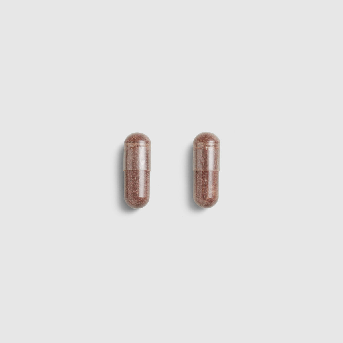 Two brown Juice Plus+ Capsules on a light gray background