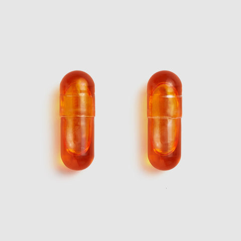 Two Juice Plus+ Omega orange capsules on a light gray background