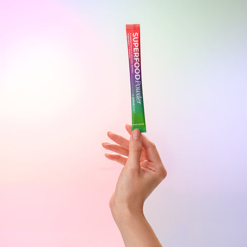 Hand holding a Juice Plus+ Superfood Powder packet against a gradient background