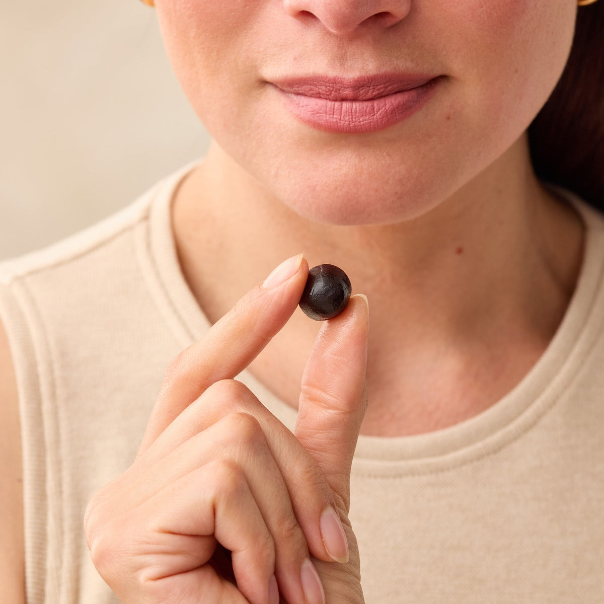 Person holding a Juice Plus+ berry Chewable between their fingers against a neutral background