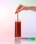 Hand stirring a glass of Juice Plus+ Superfood Powder package on a gradient background