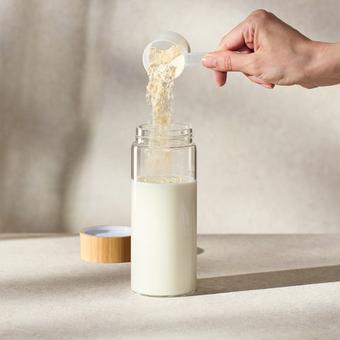Person adding Juice Plus+ Complete powder to a glass bottle of milk on a neutral background