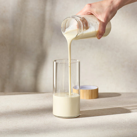 Person pouring Juice Plus+ Complete from a glass container into a glass on a neutral background