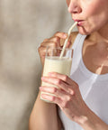 Person drinking a glass of milk with a straw against a neutral background