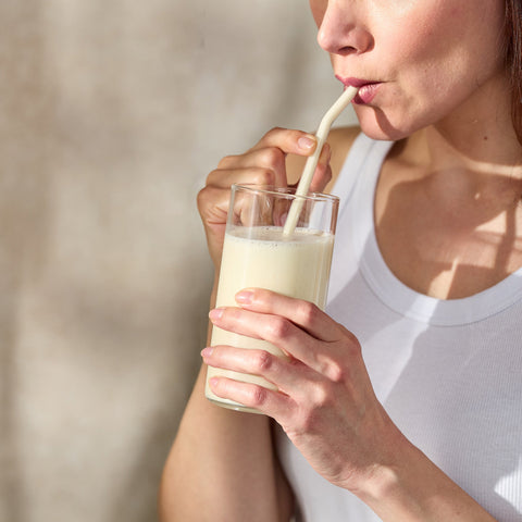 Person drinking a glass of milk with a straw against a neutral background