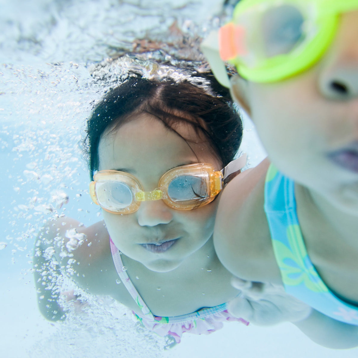 Two children wearing goggles underwater in a pool