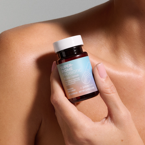 Hand holding a bottle of Juice Plus+ Super Biome Probiotic against a neutral background